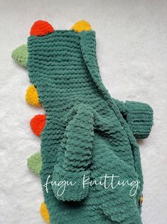 a green crocheted alligator with multi colored pom - poms on it's back