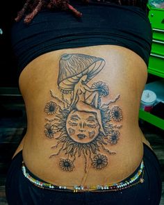 a woman's back with sun and mushroom tattoo on her lower body, in front of a green wall