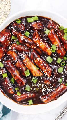 a white bowl filled with meat covered in sauce and green onions on top of a table