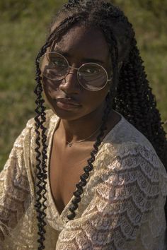 a woman with glasses and braids on her head sitting in the grass looking at the camera