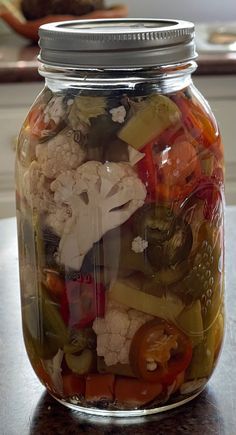 a glass jar filled with lots of different types of vegetables on top of a table