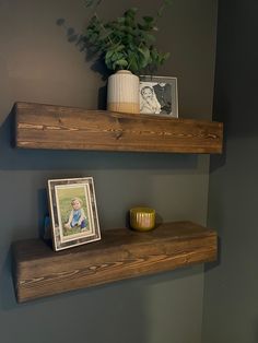 two wooden shelves with pictures on them in a small bathroom, next to a potted plant