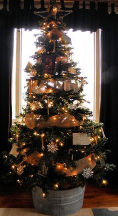 a decorated christmas tree in a bucket with lights and decorations on the top is sitting by a window