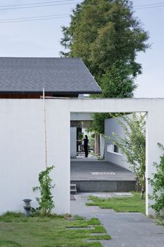 a person standing in the doorway of a white building with grass and trees around it