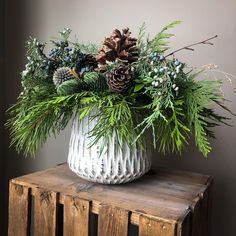 a white vase filled with pine cones and greenery on top of a wooden table