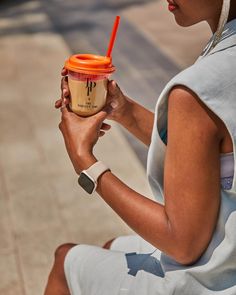 a woman sitting on the ground holding a cup with a straw in it and looking at her cell phone