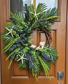 a wreath with starfishs and greenery hangs on the front door