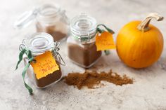 three small jars filled with spices sitting on top of a white counter next to an orange pumpkin