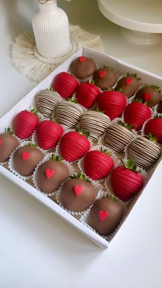 a box filled with chocolate covered strawberries on top of a white table next to a vase