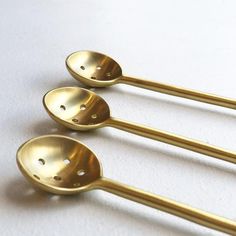 three gold spoons with holes in them on a white surface