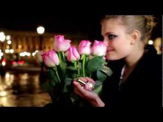 a woman holding a bunch of pink roses in her hand and looking at the camera