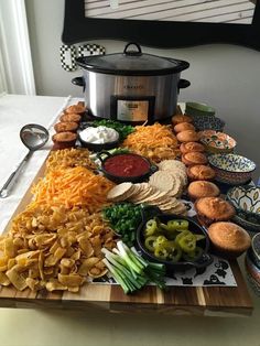 a wooden cutting board topped with different types of food next to a crock pot