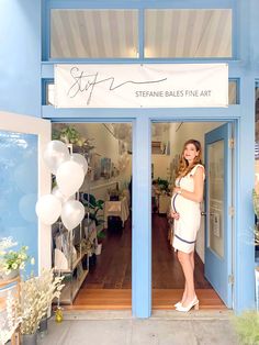 a woman standing in the doorway of a store with balloons and flowers on display behind her