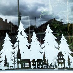 the window is decorated with white paper cutout trees and houses in front of them