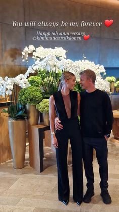 a man and woman standing next to each other in front of white flowers on display