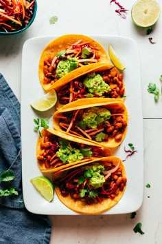 three tacos on a white plate with lime wedges and cilantro garnish