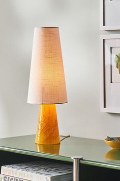 a table with a lamp on top of it next to a bowl and pictures hanging on the wall