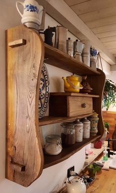 a wooden shelf filled with pots and pans on top of a wall next to a window