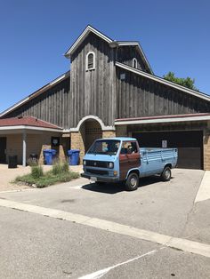 a blue truck is parked in front of a barn with a brown and white roof