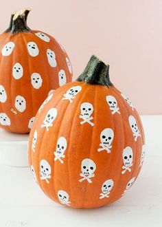 two pumpkins decorated with skulls and bones are sitting on a white surface in front of a pink wall