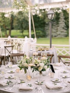 the table is set with white flowers, candles and place settings for an elegant dinner