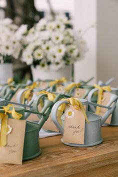 small watering cans with tags tied to them are sitting on a table in front of flowers