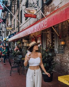 a woman walking down the street while holding an ice cream cone in her hand and wearing a straw hat