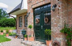 a brick house with potted plants on the front porch and green double doors to another building