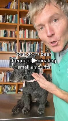 a man holding a small black dog in front of a bookshelf