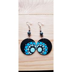 a pair of earrings with blue and black designs on them sitting on a wooden surface