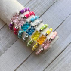 a stack of bracelets with different colored beads on top of each other, sitting on a white wooden surface