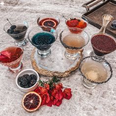 several glasses filled with different kinds of drinks on top of a marble table next to fruit