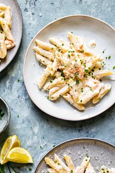 two plates filled with pasta and shrimp on top of a table next to lemon wedges