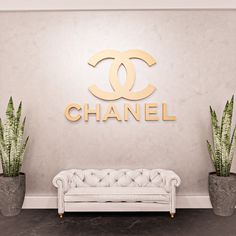 a white couch sitting in front of a chanel sign next to two potted plants