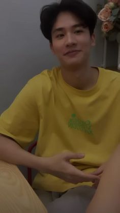 a young man sitting on top of a bed wearing a yellow shirt and black hair