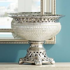 a silver bowl sitting on top of a wooden table next to a mirror and wall