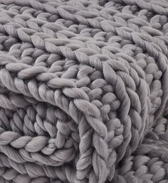 a pile of chunky knitted blankets on top of each other in shades of beige