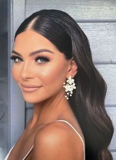 a woman with long dark hair wearing large white flowers in her hair, smiling at the camera