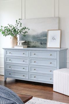 a blue dresser in a white room with a painting on the wall and a plant