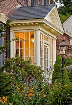 a house that is next to some bushes and flowers in front of the house,