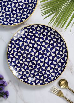 two blue and white plates sitting on top of a table next to gold utensils