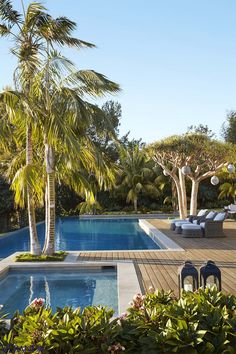 an outdoor swimming pool with lounge chairs and palm trees in the foreground, surrounded by greenery