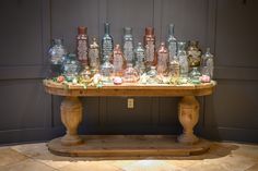 a wooden table topped with lots of glass bottles on top of a tile covered floor