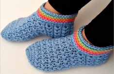 someone is wearing blue crocheted slippers with rainbow stripes