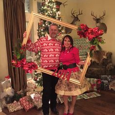 a man and woman standing in front of a christmas tree holding up a framed photo