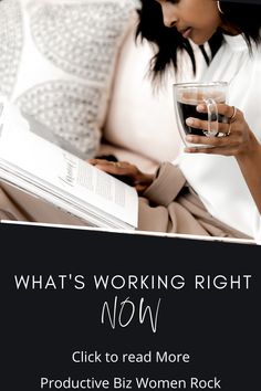 a woman sitting on a couch reading a book and holding a glass in her hand