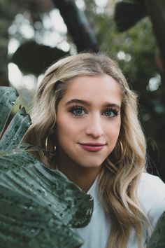 a woman with long blonde hair and blue eyes is posing for a photo in the woods