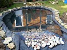 a small pond with rocks in it and an open window on the other side that is surrounded by grass