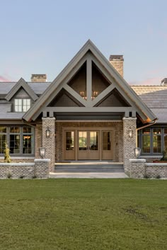 the front entrance to a large house with stone pillars and windows on each side, along with grass