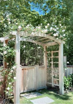 a wooden arbor with white roses growing on it's sides and an open door